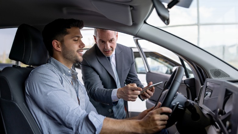 A person about to test drive a car while a salesperson explains something from the outside