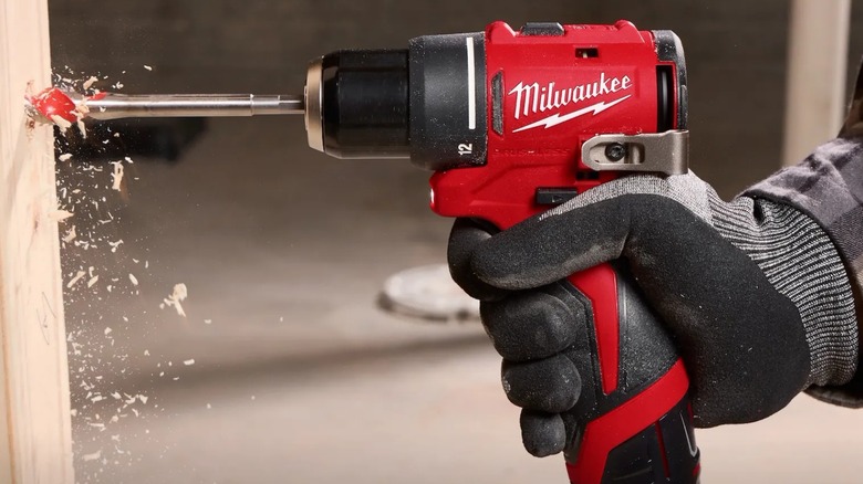 A person using a M12 Subcompact Brushless ⅜ Drill Driver on a wooden frame.