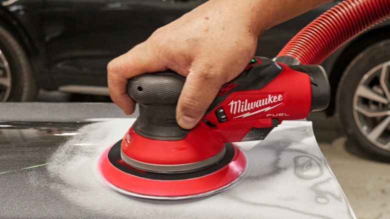 Person using M12 Fuel 6-Inch Random Orbital Sander on car hood.