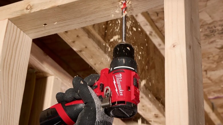 A person using an M12 Subcompact Brushless ⅜-Inch Drill/Driver on a wooden frame.