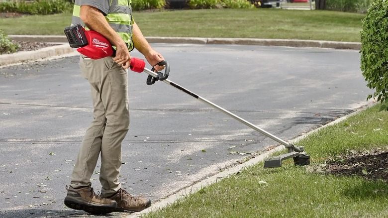 A person using an M18 Fuel 16-Inch String Trimmer on grass.