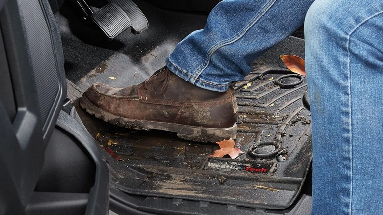 A person's muddy boots on a set of Weathertech floor mats