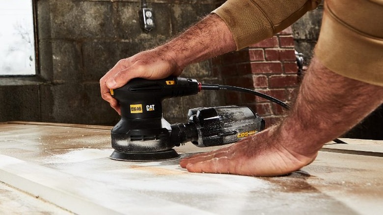 man holding Cat 5-inch Random Orbit Sander