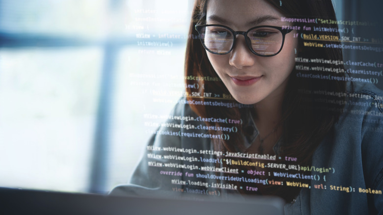 Female programmer looking at a computer screen with computer code super-imposed in the foreground.