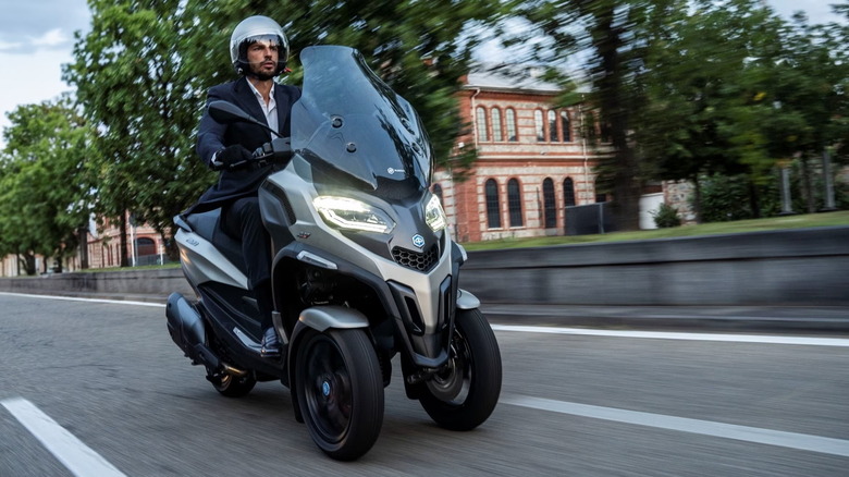 Silver Piaggio MP3 scooter on city street with rider in suit