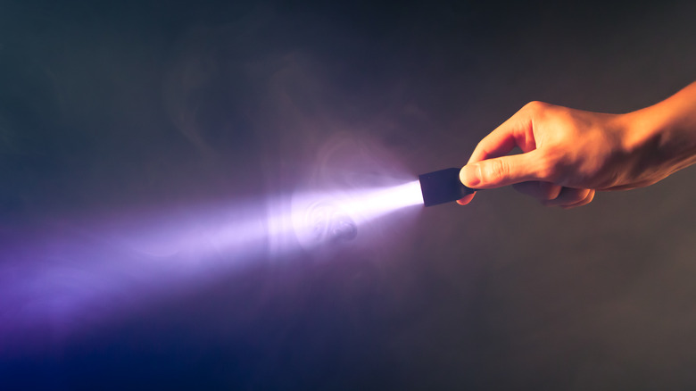 Hand holding a shining flashlight in dark room