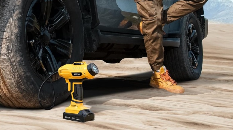 An AstroAI portable tire inflator being used to fill a tire while a driver leans against the car