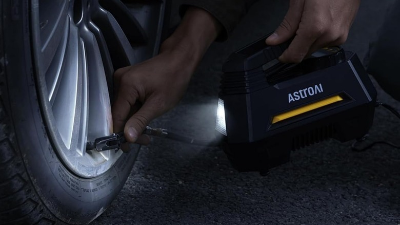 A close-up of a person using an AstroAI portable tire inflator to inflate their car tire