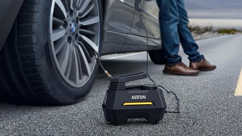 An AstroAI portable tire inflator being used to fill up a tire while the driver leans against the car