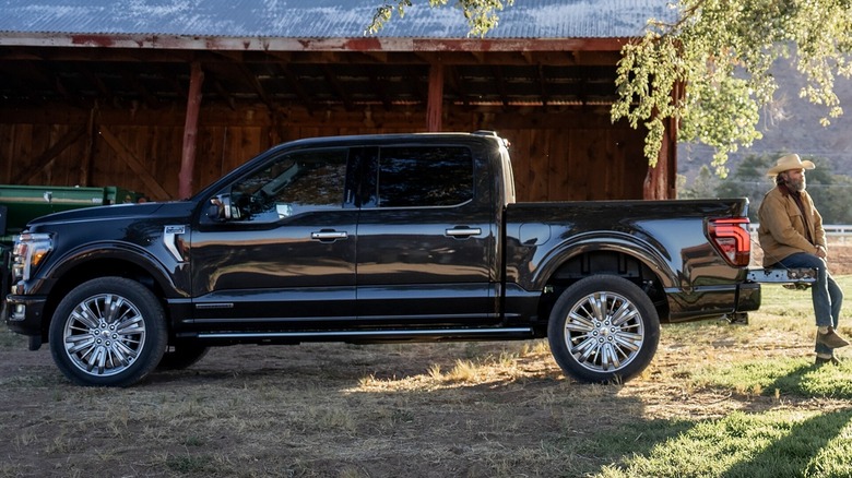 A black 2025 Ford F-150 parked near a barn with a man resting on the tailgate.