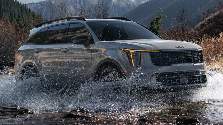 2025 Kia Sorento driving through a shallow river with mountains in the background