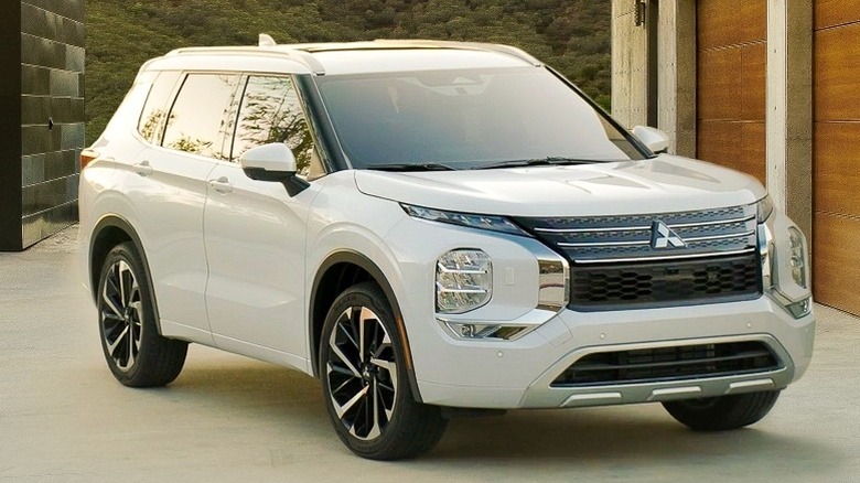 2022-24 Mitsubishi Outlander parked on a paved driveway in front of a house with trees and hills in the background