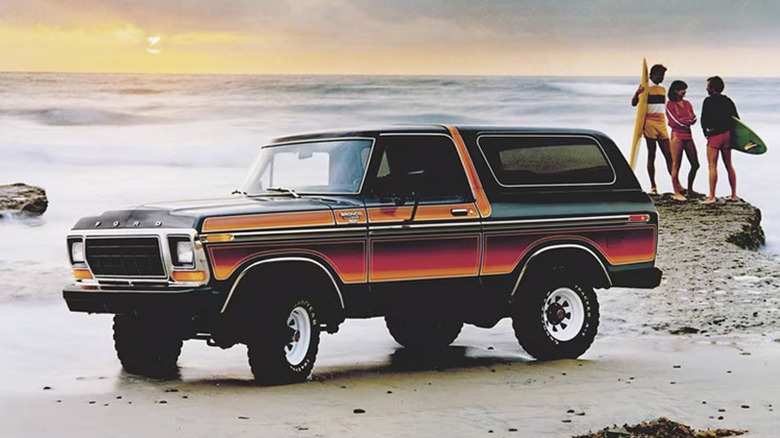 Late '70s Ford Bronco with Free-Wheeling multicolor striping parked on beach with three young surfers in background