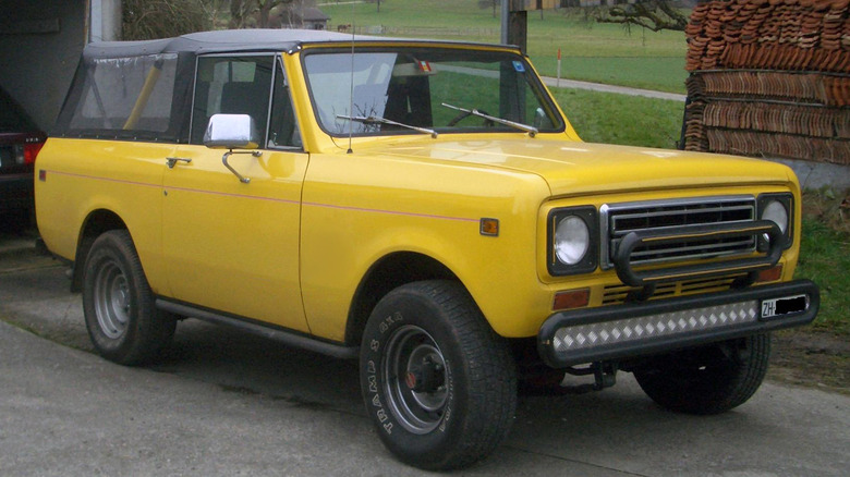 Yellow International Scout II with black soft top parked in front of brick wall next to golf course