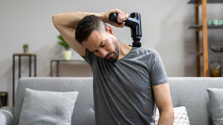 man using massage gun on shoulder