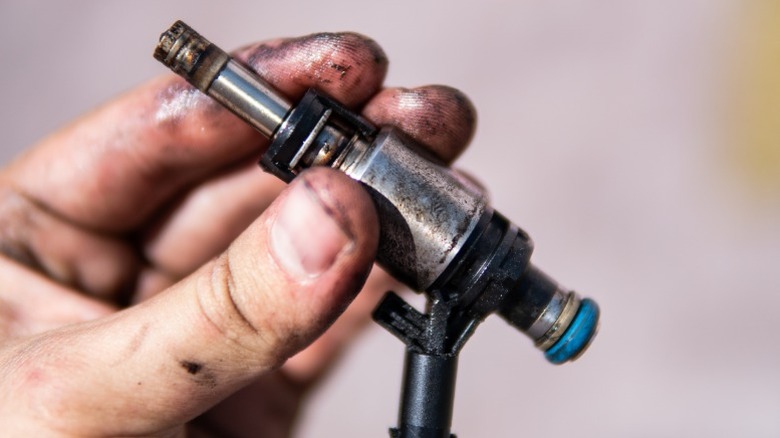 A person holding an old potentially clogged fuel injector