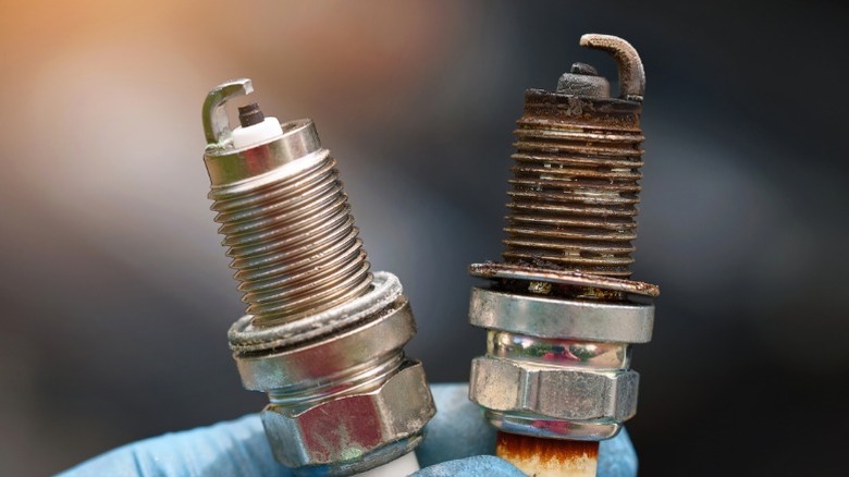 A closeup image of someone holding one new and one bad spark plug