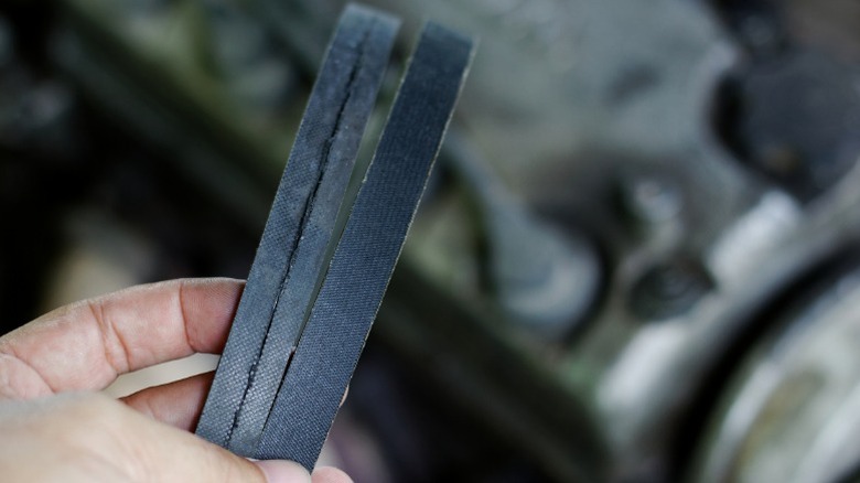 A person holding a severely cracked serpentine belt next to a new belt