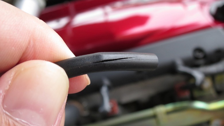 A person holding a cracked engine vacuum hose