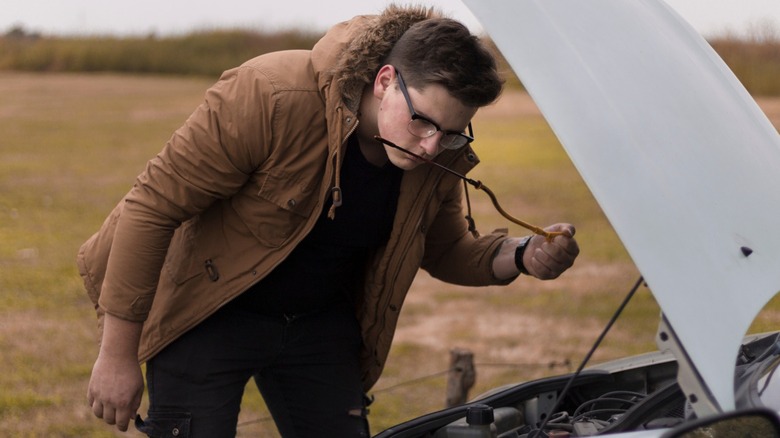 A person smelling their engine oil dipstick