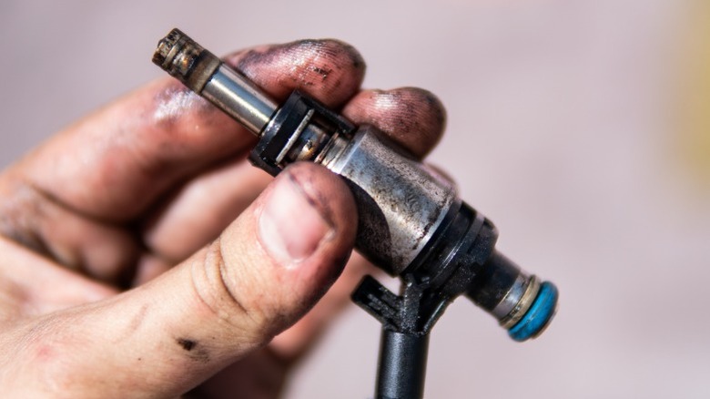 A person holding an old dirty fuel injector