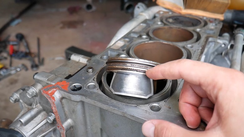 A person showing damaged piston rings on a disassembled engine