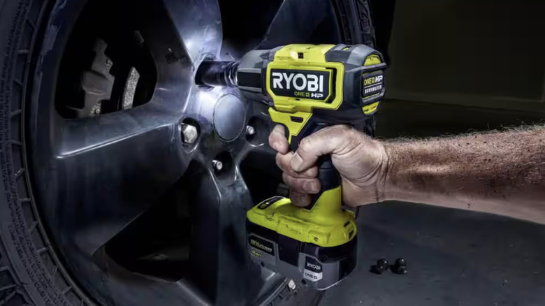 A person using an impact wrench on a wheel's lug nuts