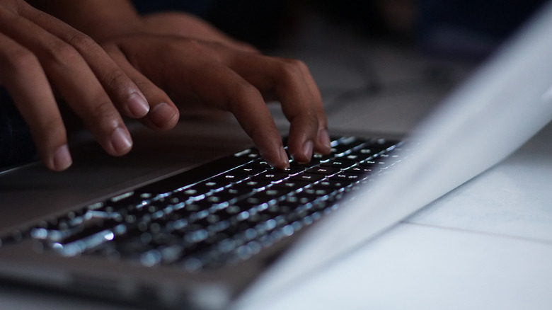 person typing on a MacBook with backlit keyboard