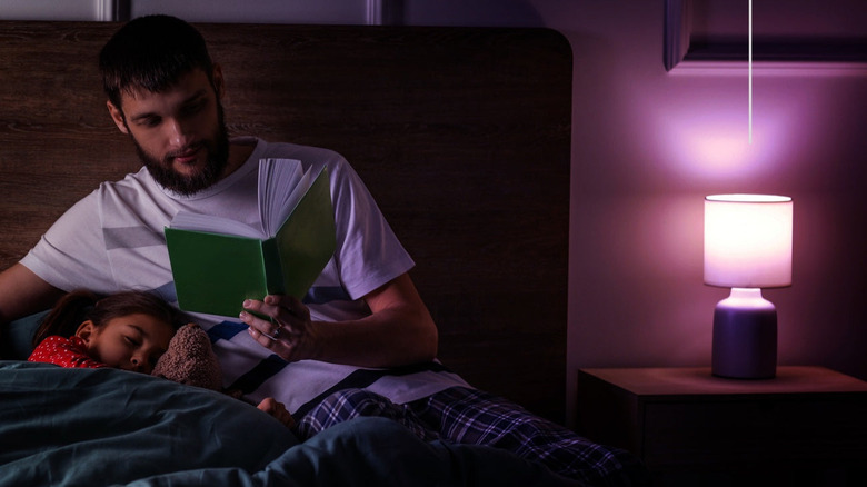 A father reads to his daughter near a LIFX light bulb