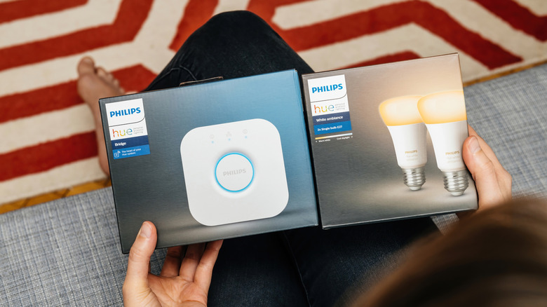 Woman sitting on couch holding packaged Philips Hue bulbs and hub