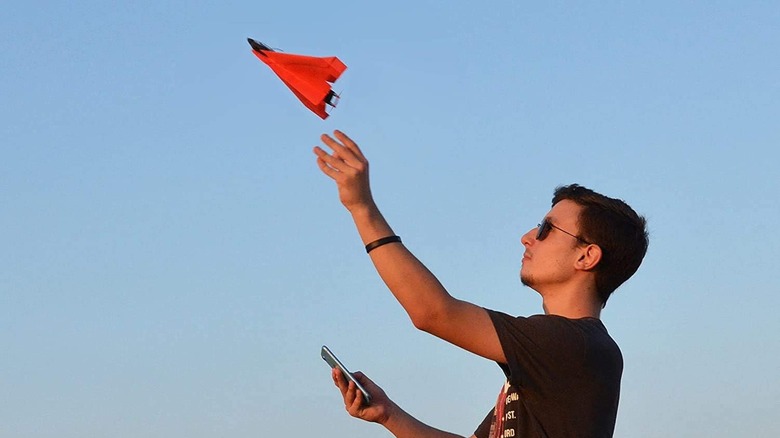 Man throwing red paper plane into air