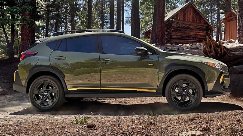 Alpine green Subaru Crosstrek Sport parked in the woods with cabins in the background