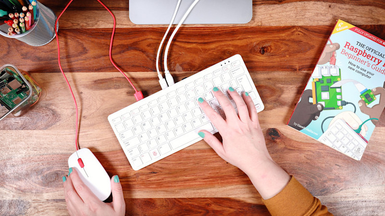 Hand using Raspberry Pi keyboard and mouse with guide book close by