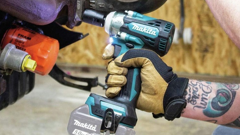 A person using an 18-volt cordless Makita 1/2-inch impact wrench on an engine turbo