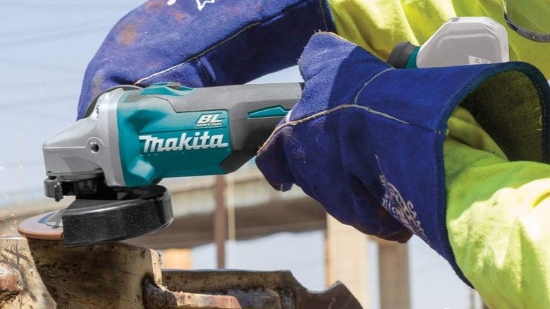 A person using an 18-volt cordless Makita angle grinder on a piece of metal