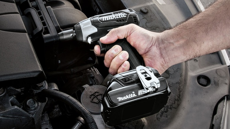 A person using a Makita impact wrench in a car's engine bay