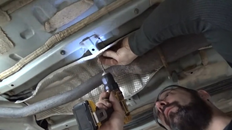 A person fixing a rattling exhaust heat shield