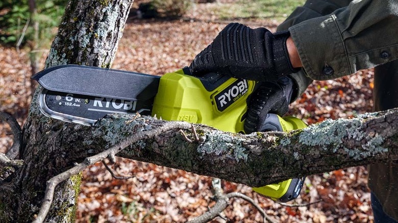 Man using Ryobi mini chainsaw on branch