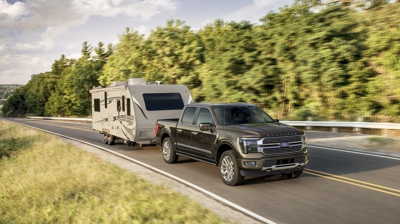 Dark Grey 2025 Ford F150 with SuperCrew cab towing large bumper-pull RV trailer on tree-lined highway