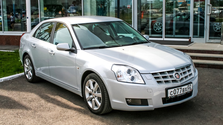 A Cadillac BLS in silver outside a dealership, front 3/4 view