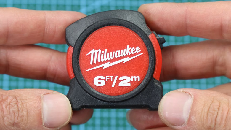 Two hands holding Milwaukee tape measure over cutting board