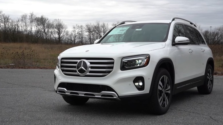 White 2025 Mercedes-Benz GLB 250 SUV parked with a dry grass field and trees in the background