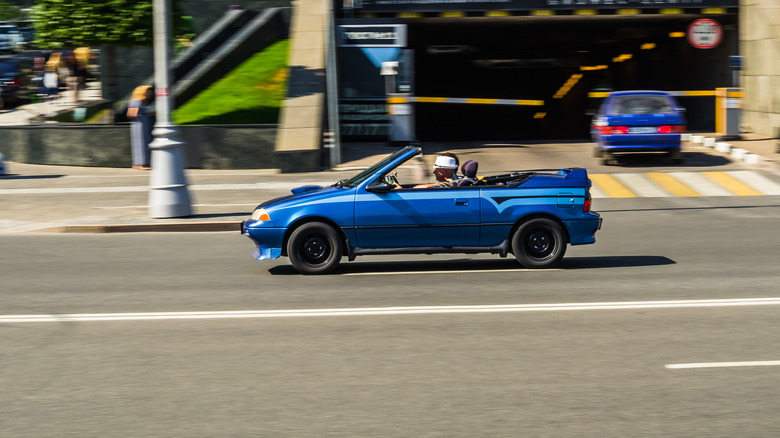 A Blue Geo Metro driving quickly up the street