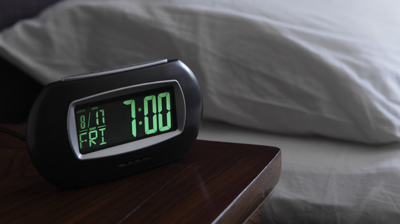 Digital alarm clock next to a bed.