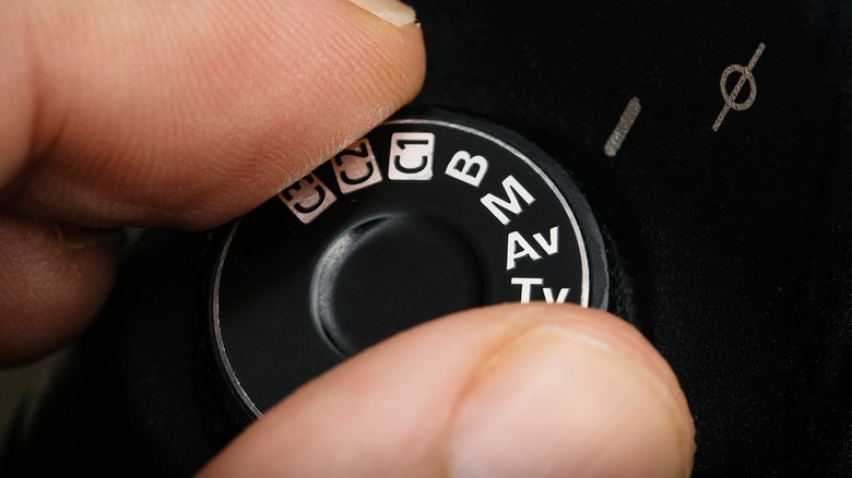 Fingers changing a DSLR dial to manual mode