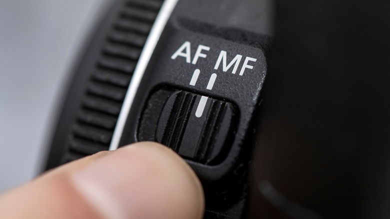 A finger sets the manual focus setting on a camera lens