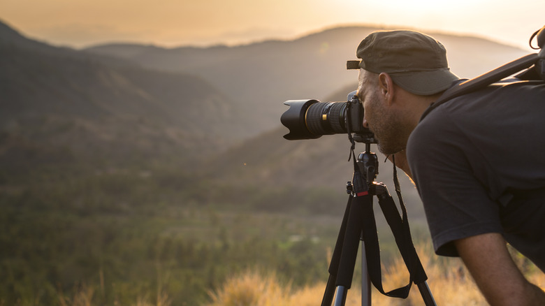 Man looking through viewfinder of camera on tripod