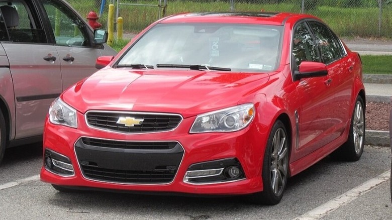 Red Chevrolet SS Sedan sandwiched between two vehicles in a parking lot