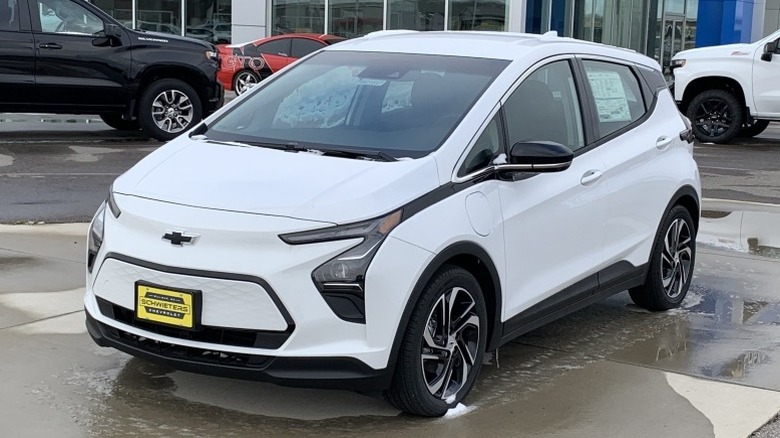 White 2022 Chevrolet Bolt parked in front of a building with other vehicles in the background