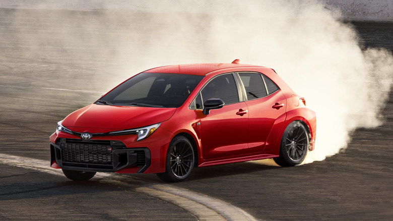 A red Toyota GR Corolla doing powerslide on a skid pad, front 3/4 view